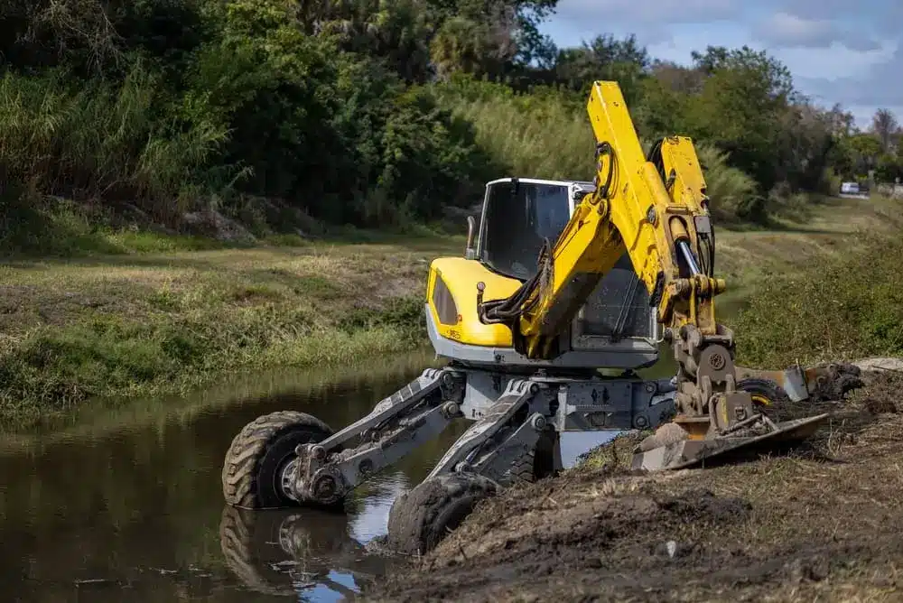 Une excavatrice ambulante jaune Menzi Muck positionnée sur la berge boueuse d'un canal.