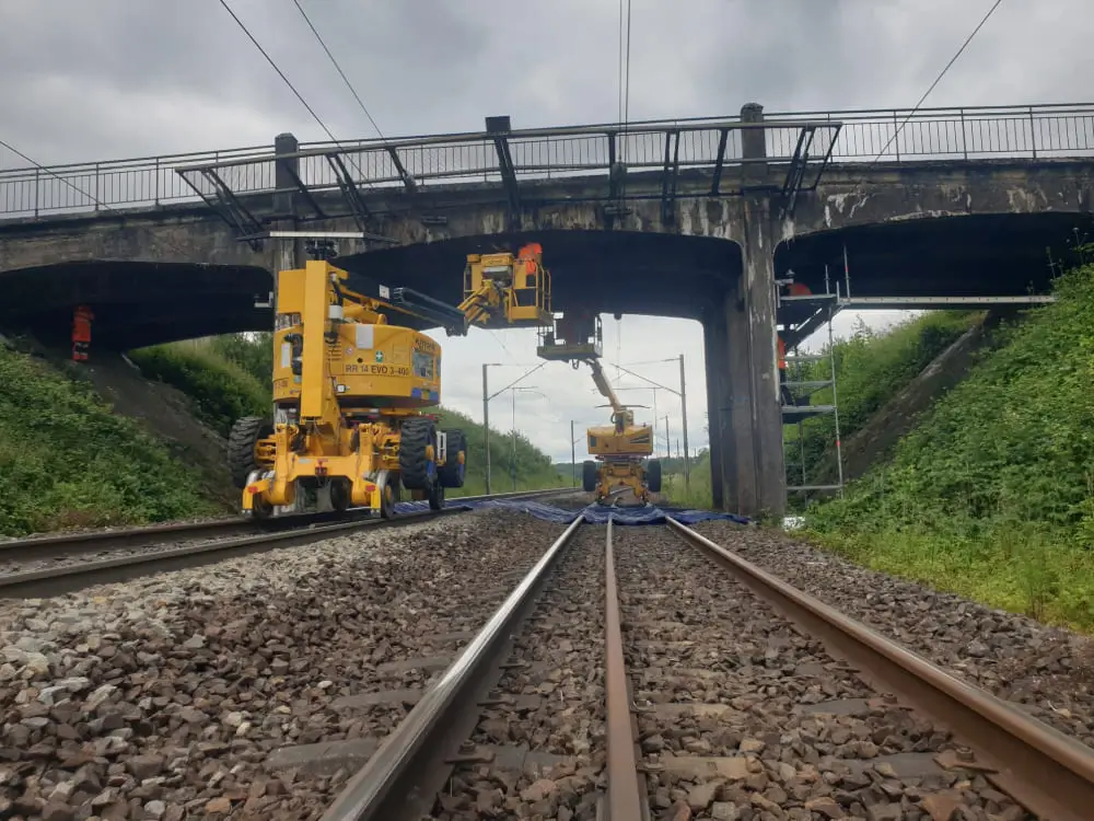 Un ouvrier du bâtiment travaille sur les voies ferrées, portant un casque et utilisant des outils de construction.