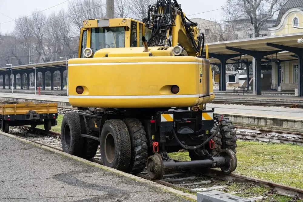 Une lourde pelle jaune sur rail stationnée sur des titres ferroviaires à côté d'une plate-forme de gare.