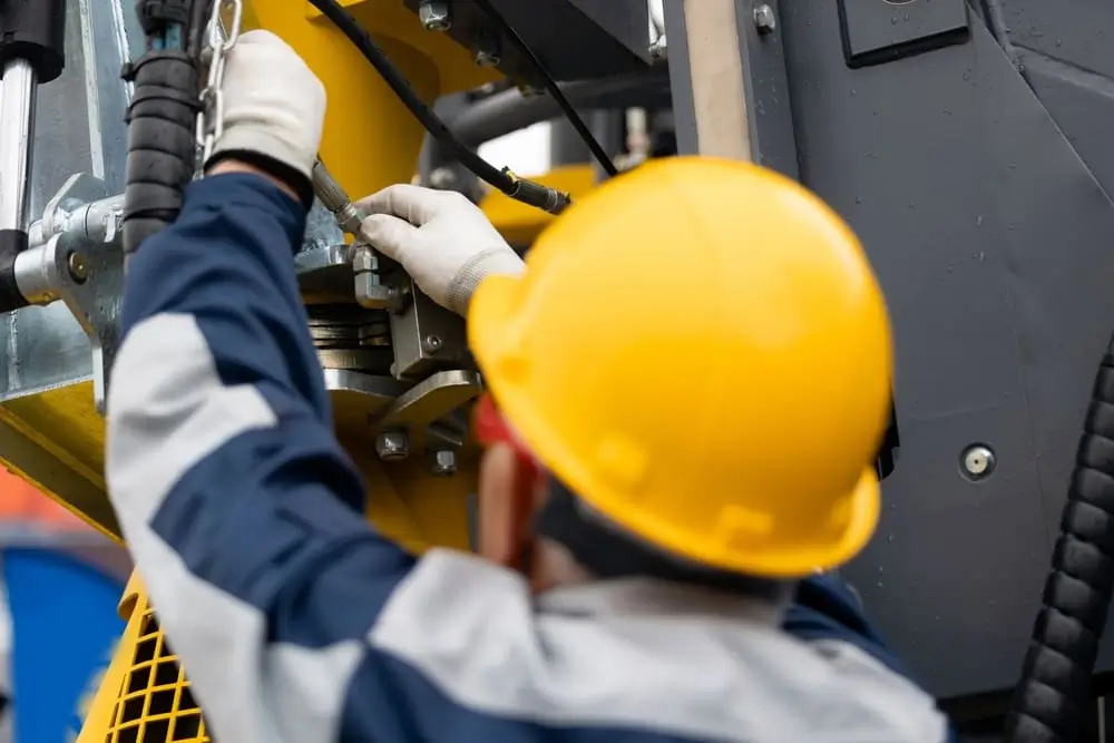 Mécanicien réparant un flexible hydraulique sur une foreuse, forage d'exploration. Homme adulte portant un casque de chantier.