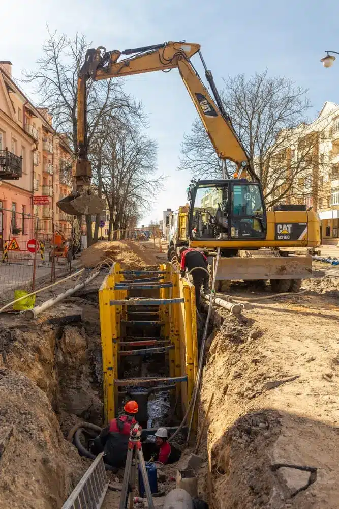 Excavateur remplissant une excavation profonde soutenue par une boîte de tranchée avec du gravier de pois pour le lit de tuyau pendant l'installation du tuyau de drainage.